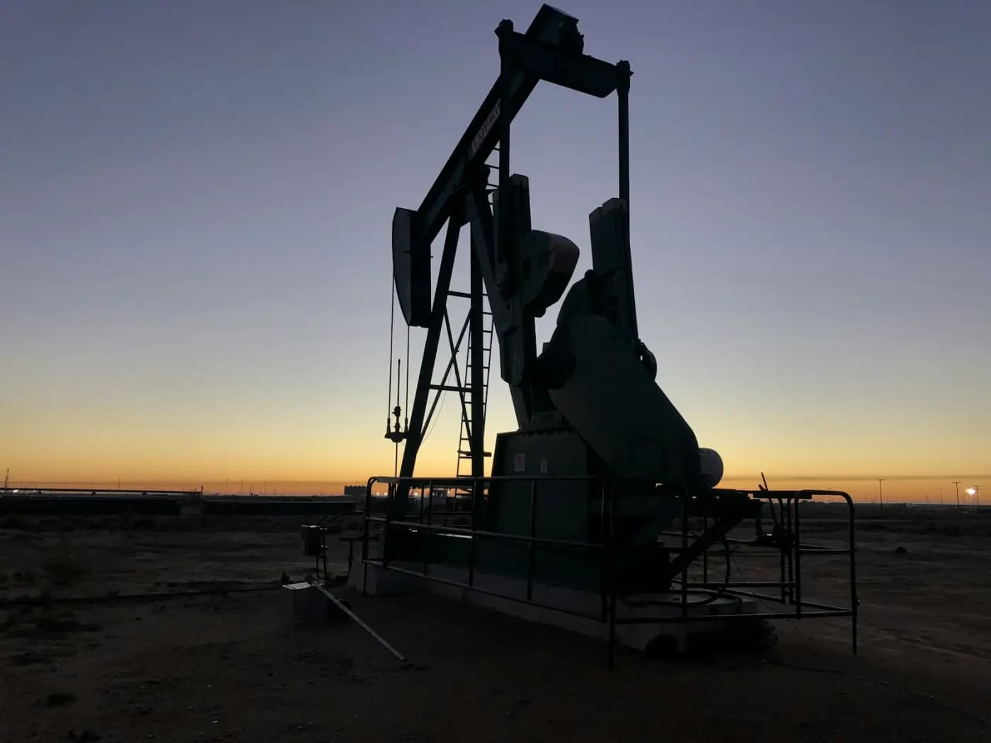Oil pumpjack silhouetted against an orange dusk sky